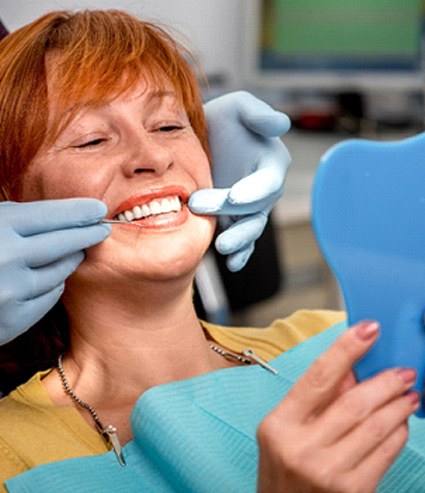 A senior woman admiring her dentures in a hand mirror